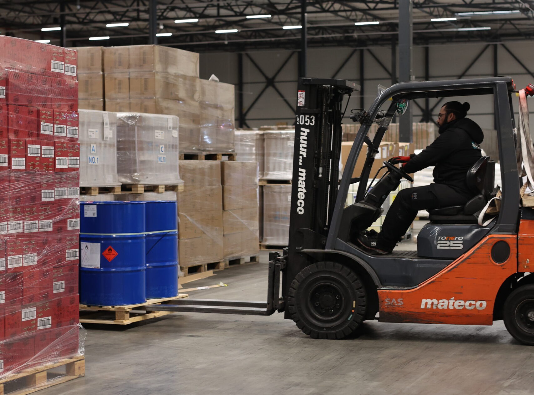 Man driving on forklift about to lift up blue barrels on pallet